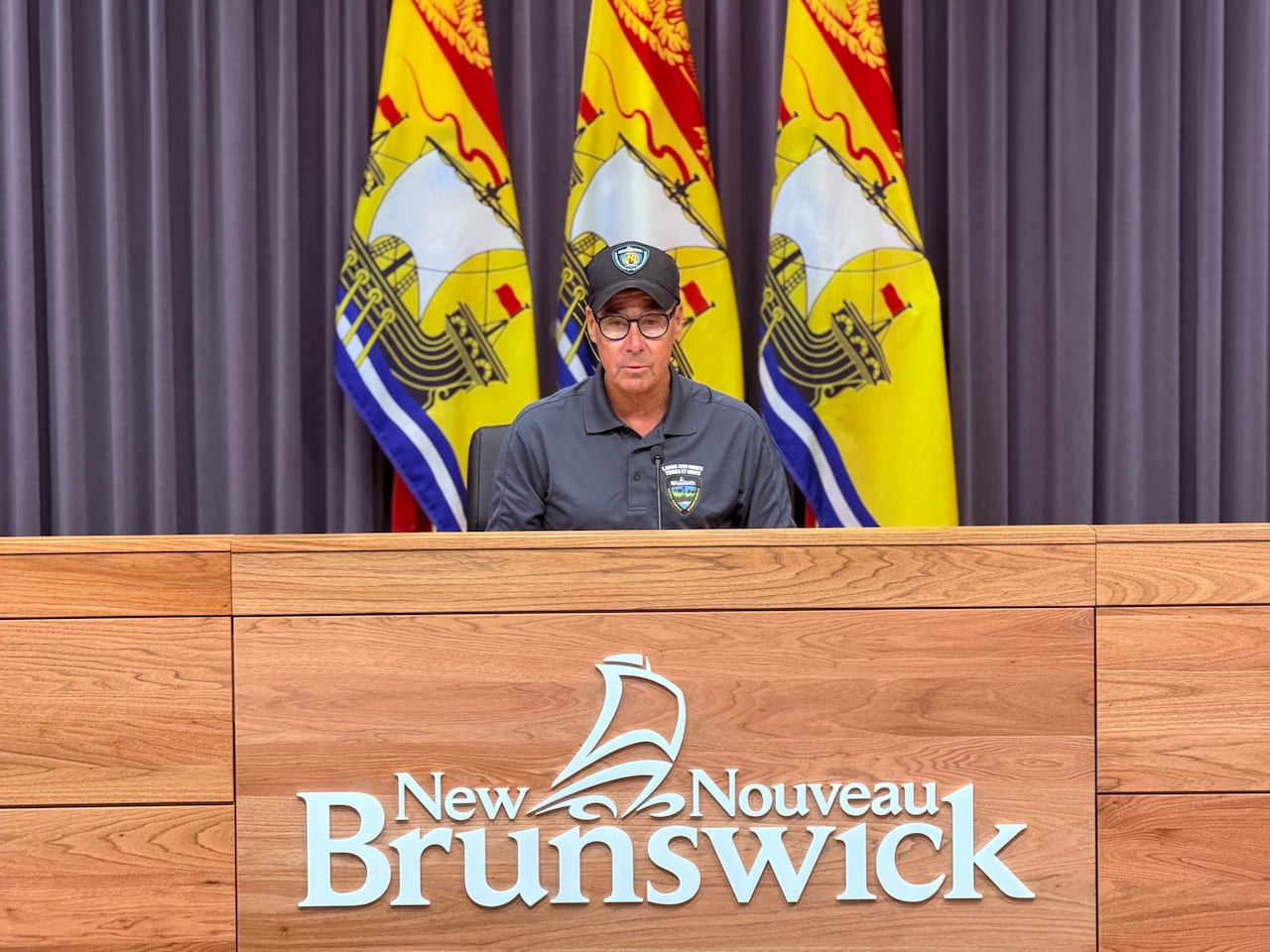 Man sits at a desk in front of a mic with a ball cap on.