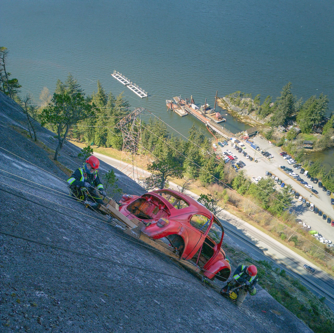 People in high-vis vests are seen suspended near a car hung on a rock face.