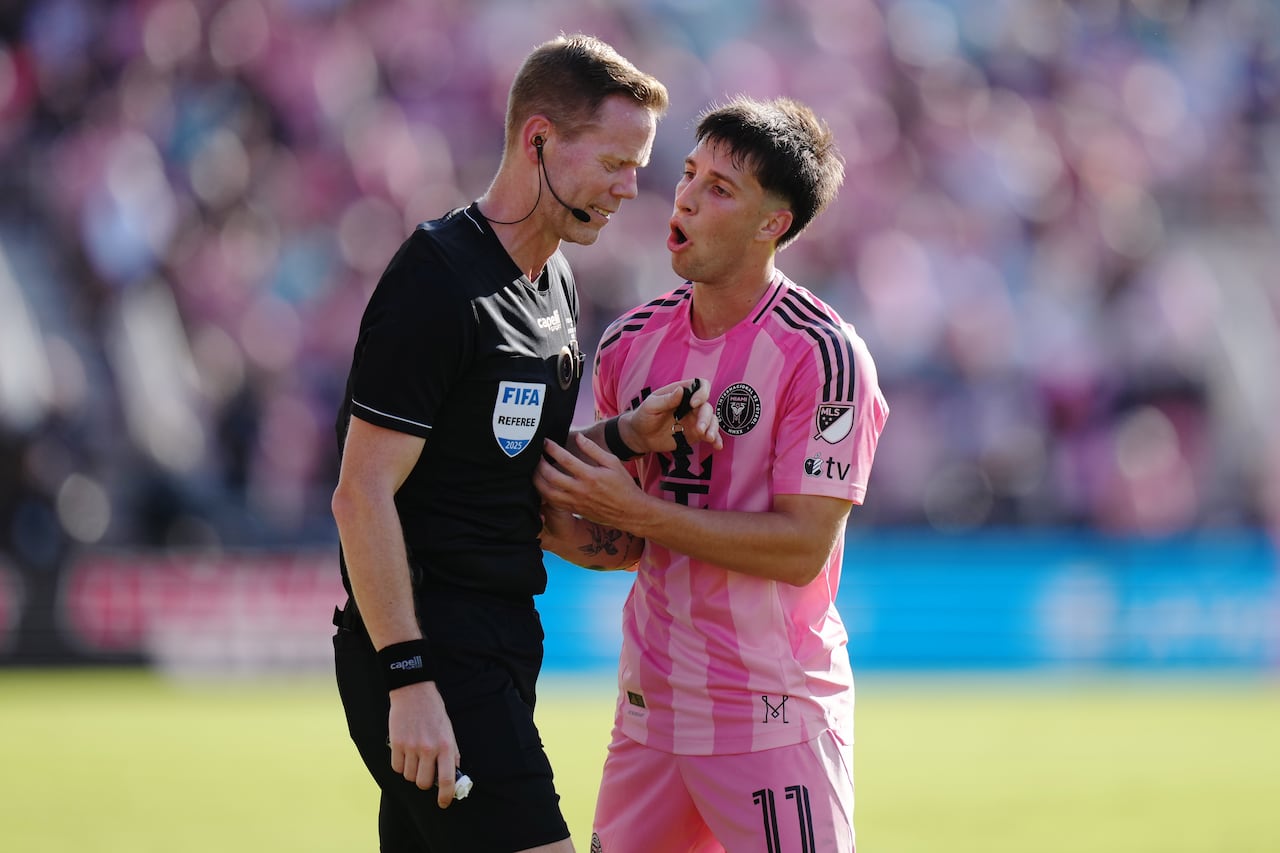 Two men on a soccer pitch, one in black and the other in a pink outfit.