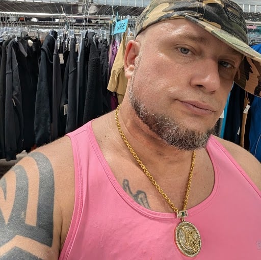 A man in a camo hat and pink tank top with a gold chain
