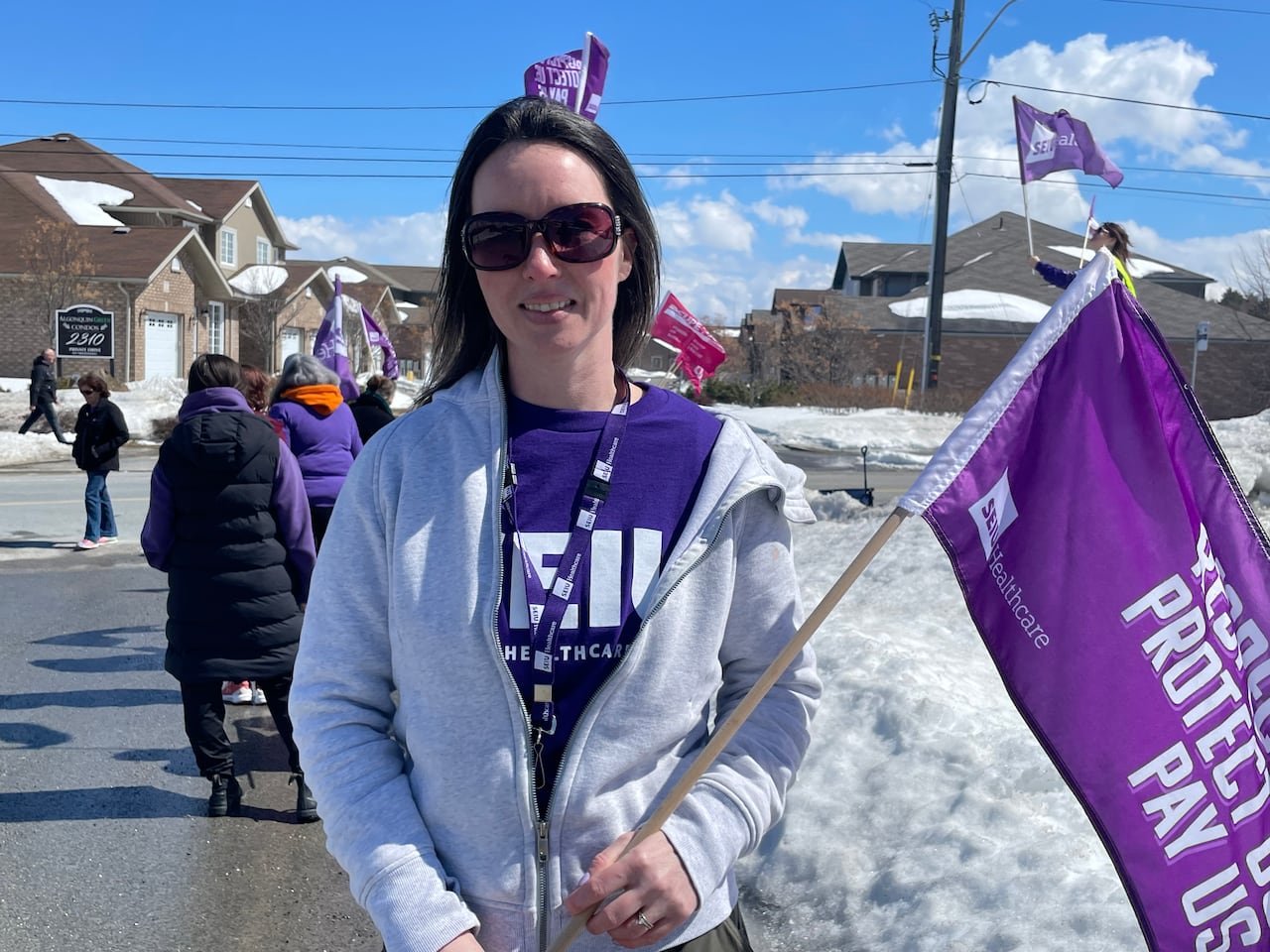 A woman wearing a grey hoodie with a purple T-shirt with a union slogan on it, holding a purple flag.