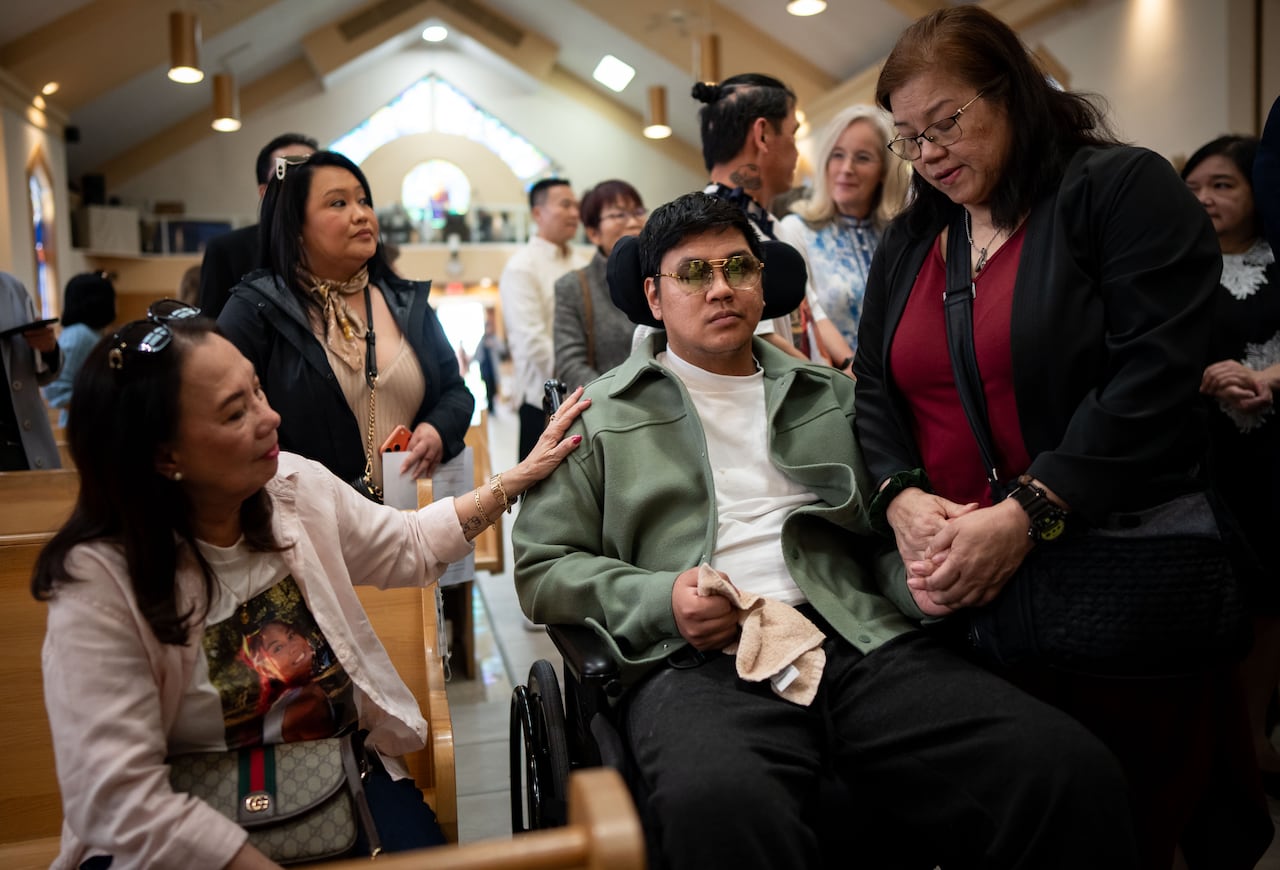 A man in a wheelchair is comforted by others in a church.