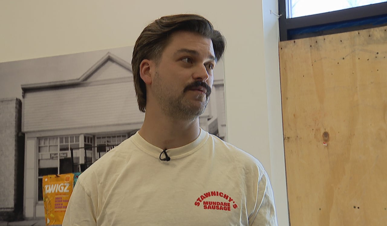 A man in a white shirt stands in front of a doorway covered by a piece of plywood. 