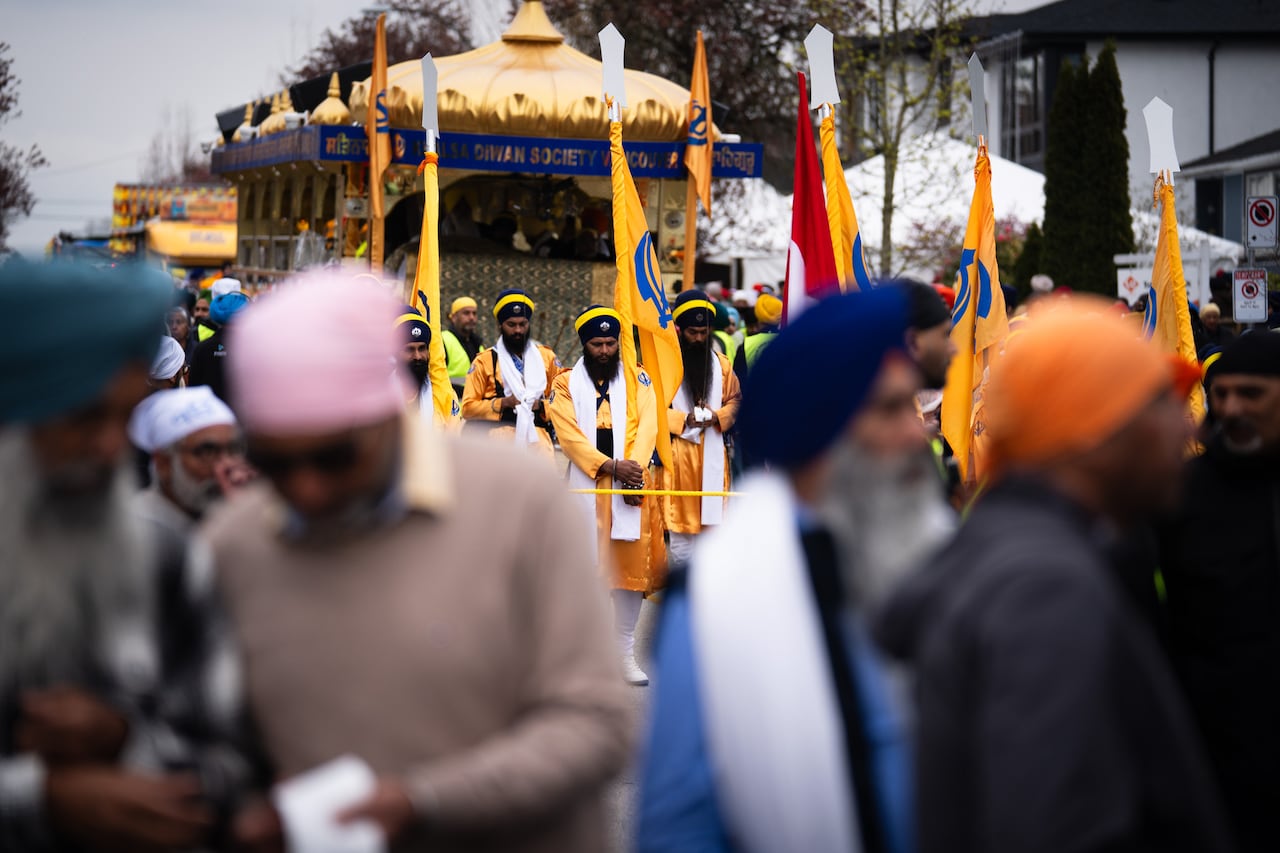 People in traditional attire carry flags during a religious procession, with a decorated float and a crowd gathered around.