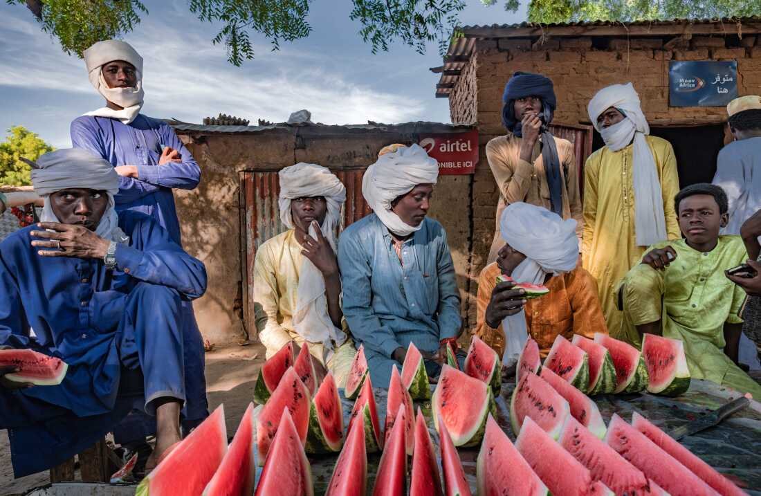 Young men eat slices of watermelon at a vendor's stall in a market in the village of Karnak, Chad. The village has seen Great Green Wall interventions from an NGO looking to plant acacia trees.