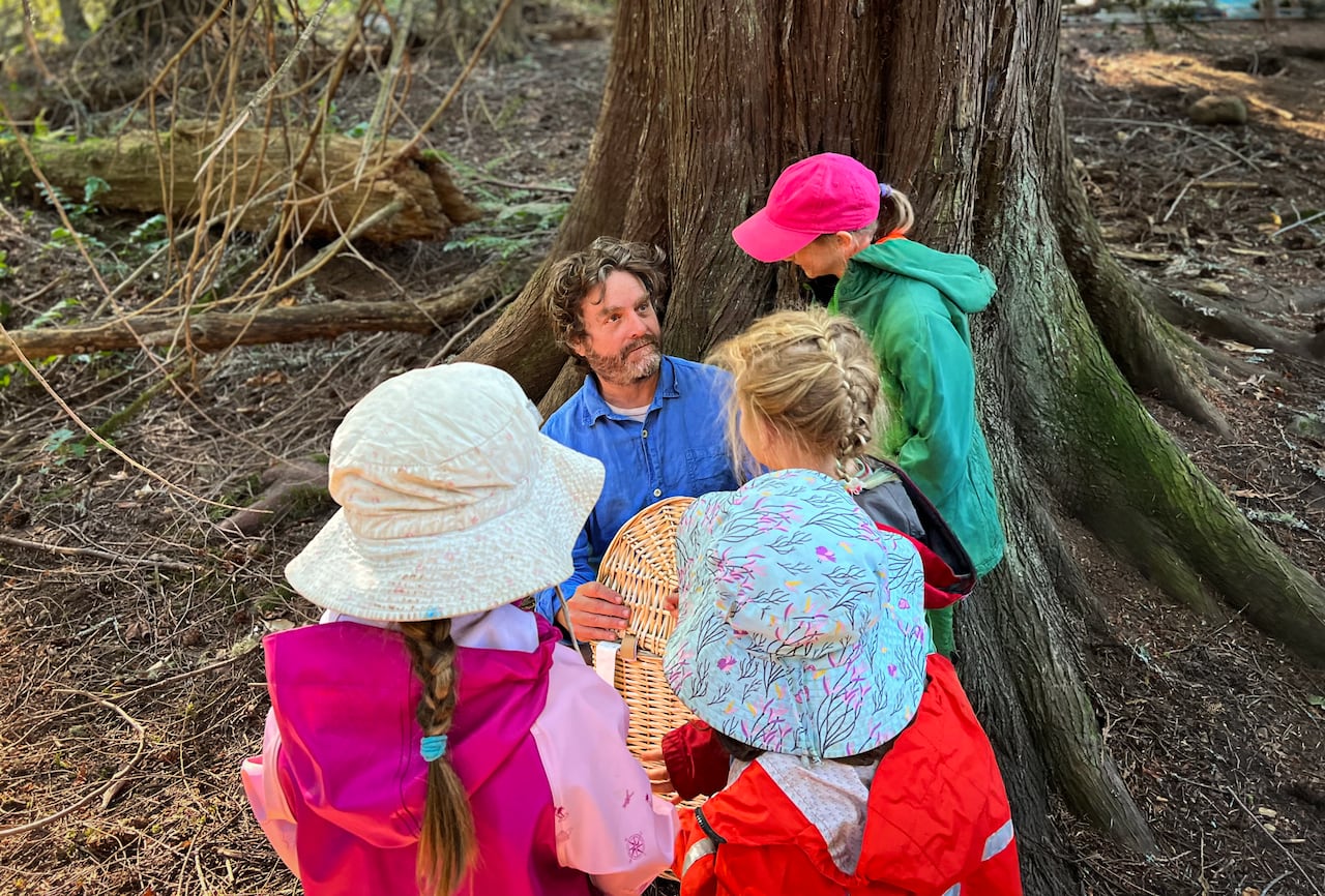 A man sits at the base of a tree with four young kids surrounding him.