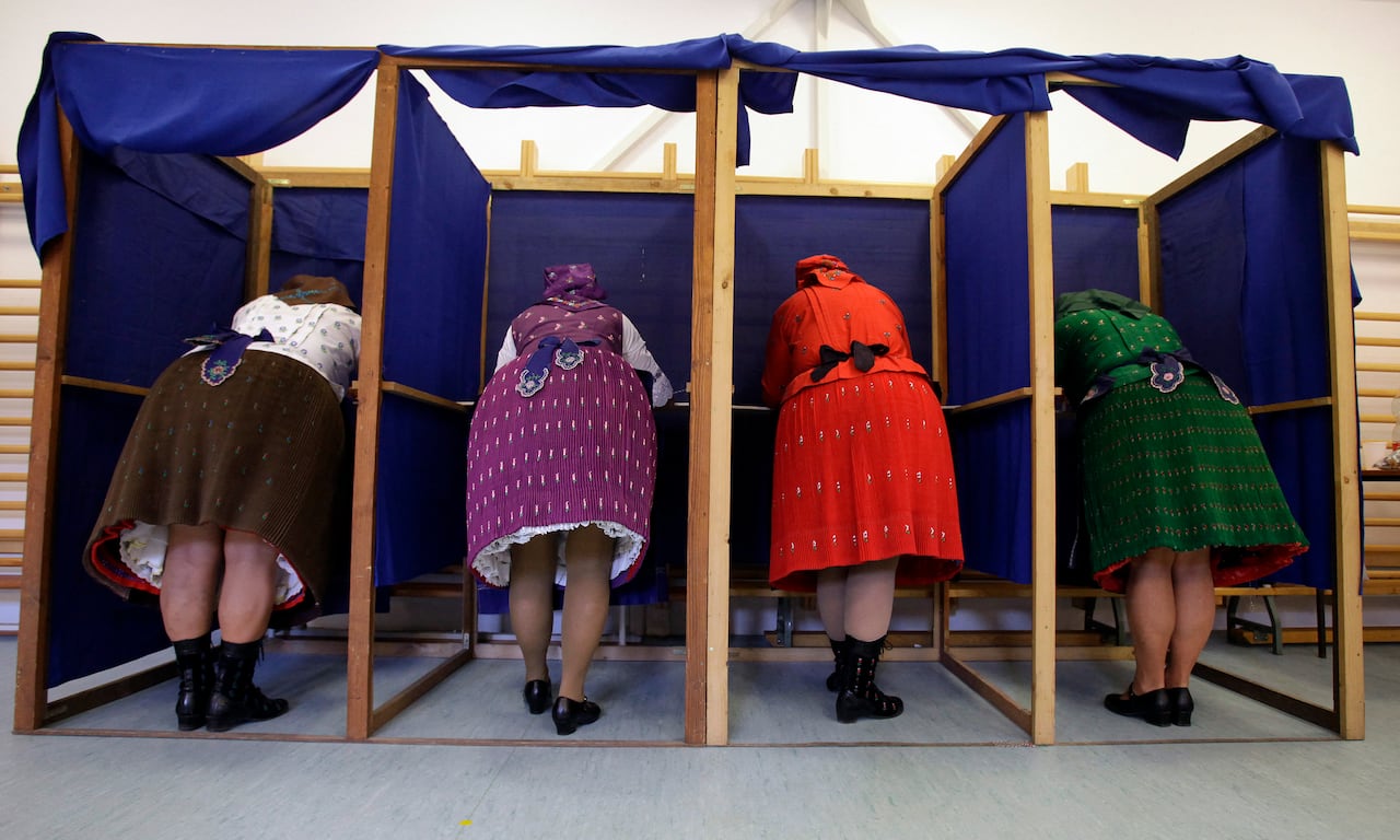 Voters in traditional Hungarian dresses fill out ballot in a polling station.