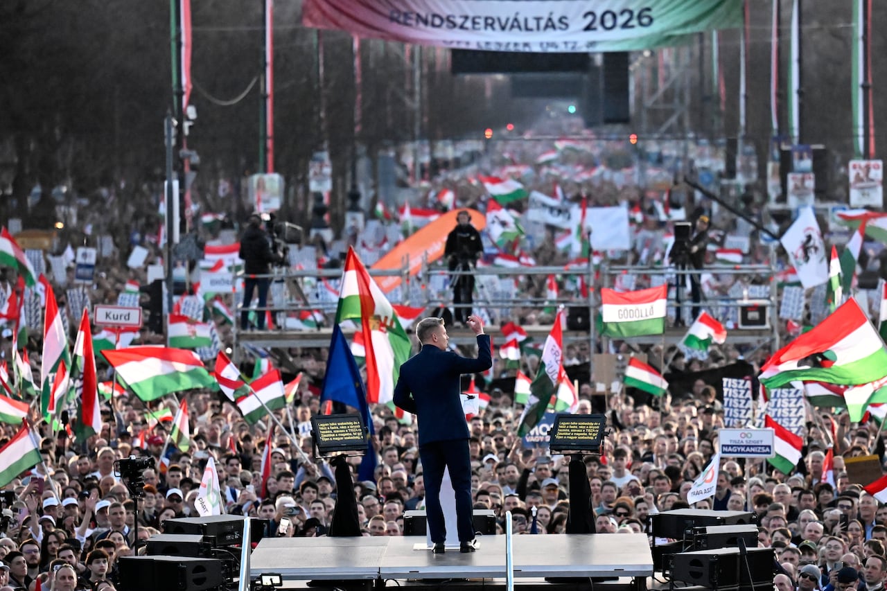 A person on a stage addresses a crowd of flag-waving supporters.