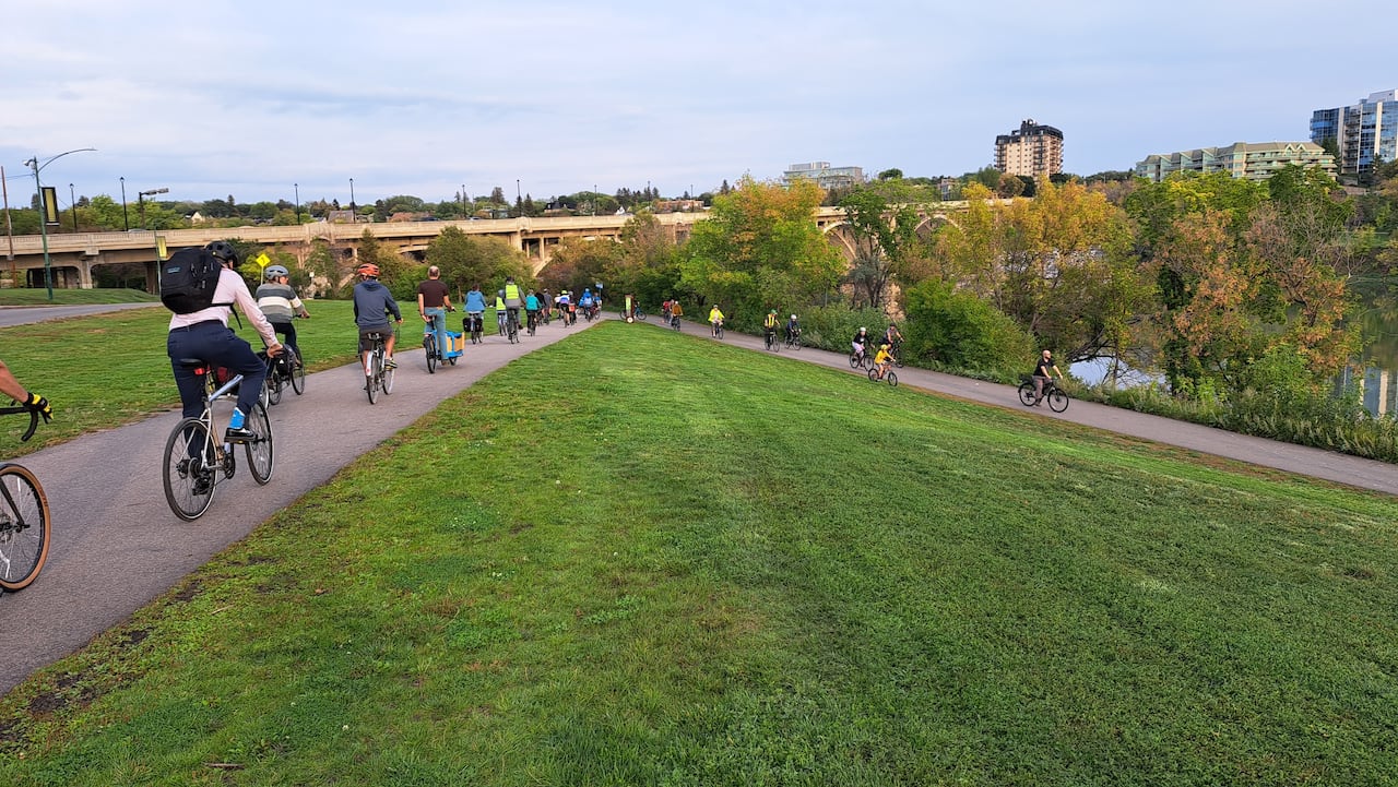 Several bikers on a park biking path, near one of Saskatoon's bridges