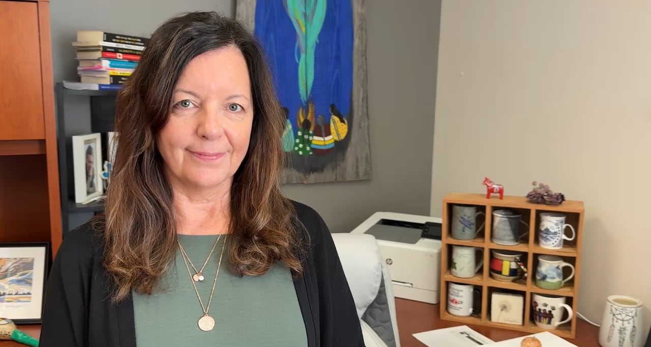 A woman with long, dark hair and a green shirt stands in an office. 