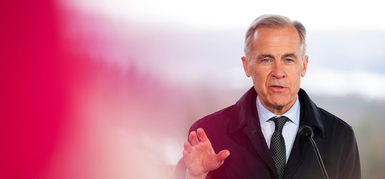 A photo on a man in a coat and a tie standing it front of a microphone talking.