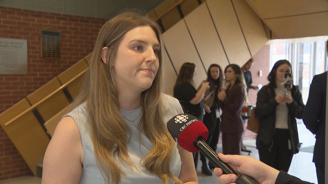 A woman in a blue shirt takes questions from a reporter.