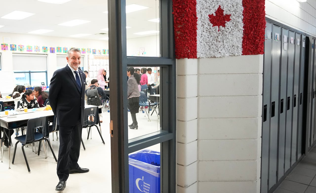 The minister stands inside a classroom that has a Canadian flag attached to the entrance.