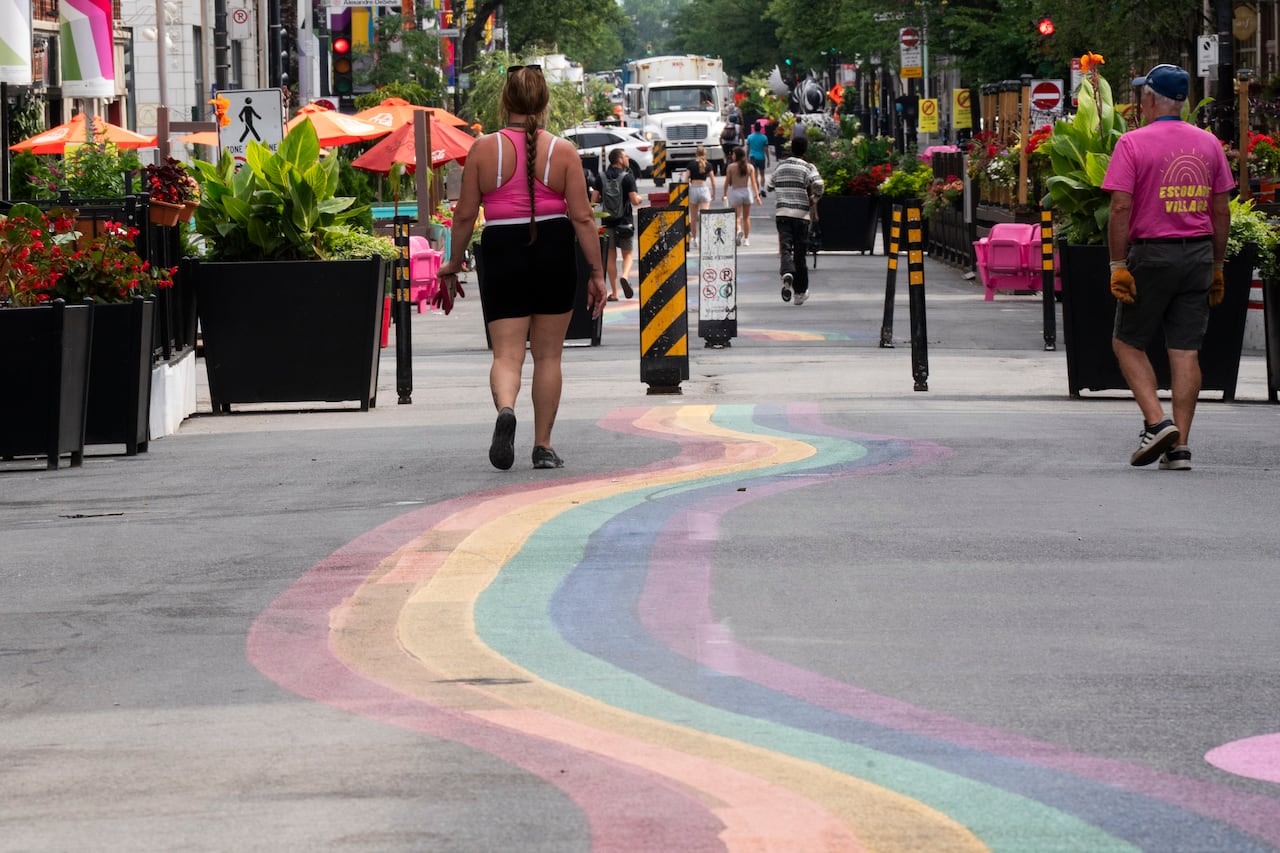 Pedestrians shown walking on street with a rainbow painted on the ground.