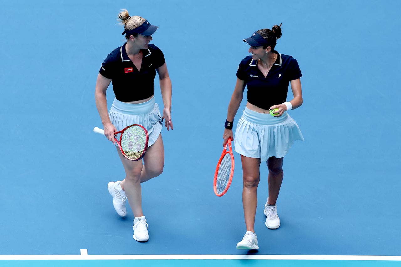 Two female tennis players speak to each other while on the court.