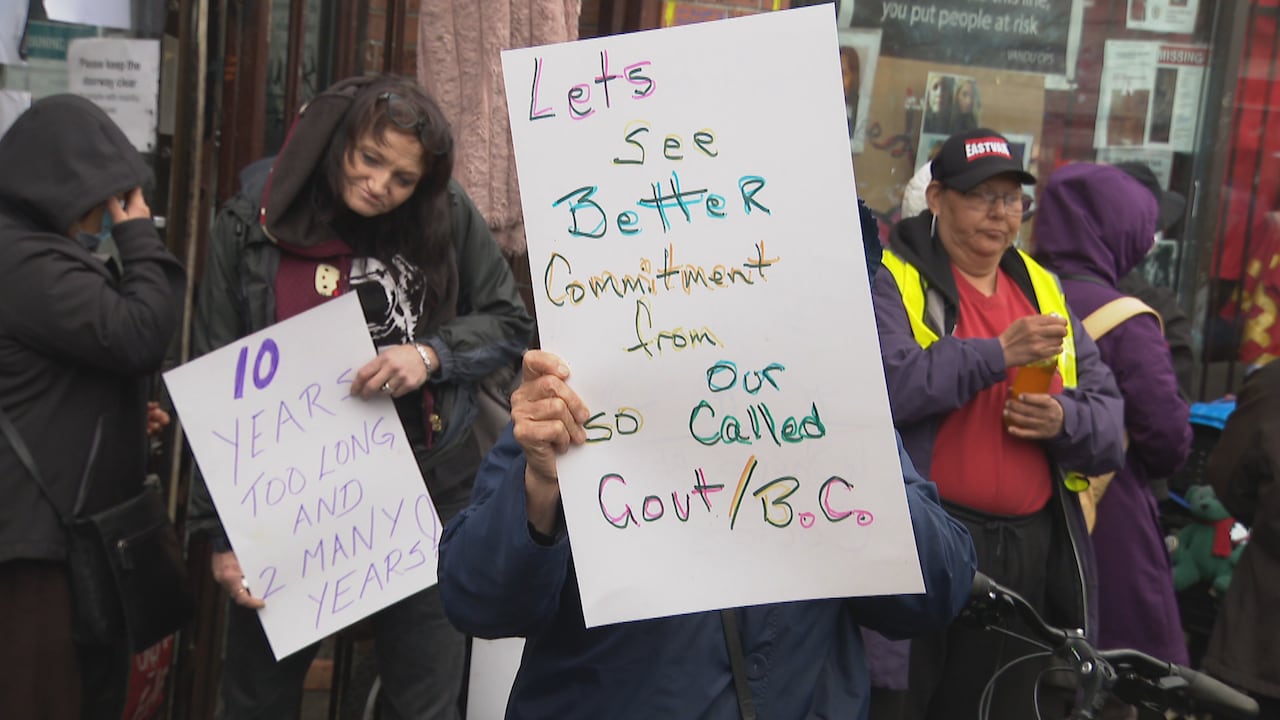 people hold up signs reading '10 years too long and 2 many years!' and 'Let's see better commitment from so our called govt/B.C.' at a rally