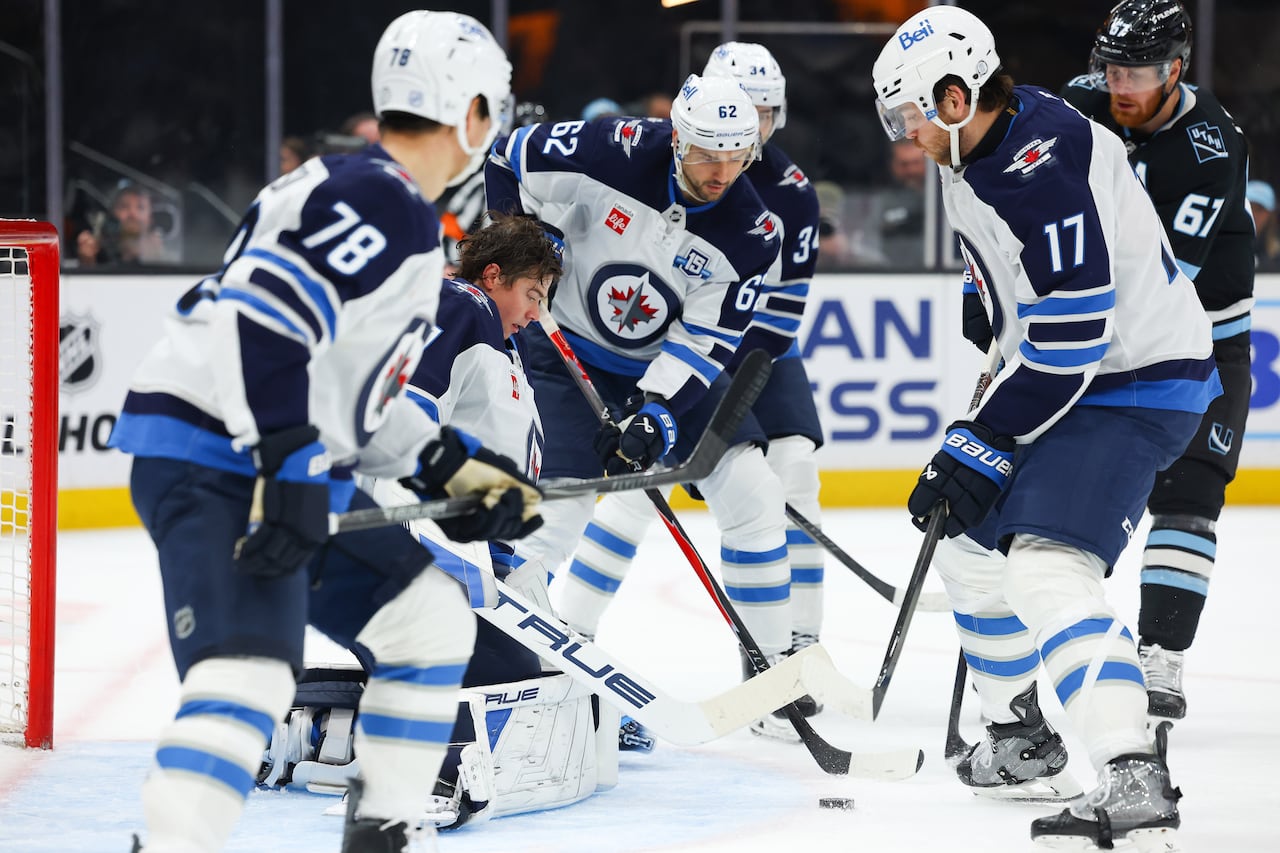 Four Jets teammates surround Winnipeg's goaltender, who isn't wearing his helmet.