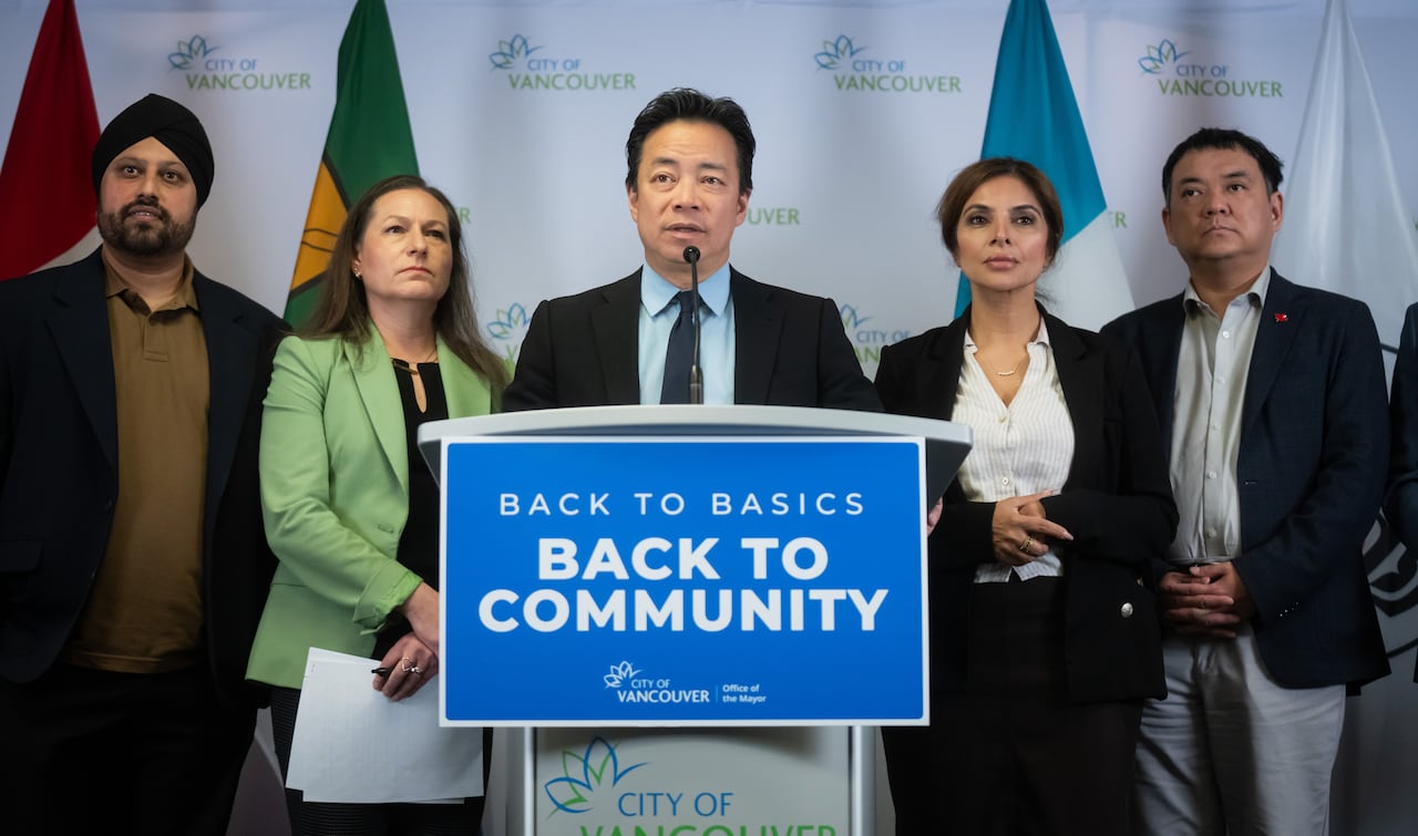 A group of three men and two women stand at a podium marked 'back to basics, back to community'.