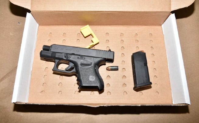 A black handgun in an open cardboard box, next to ammunition