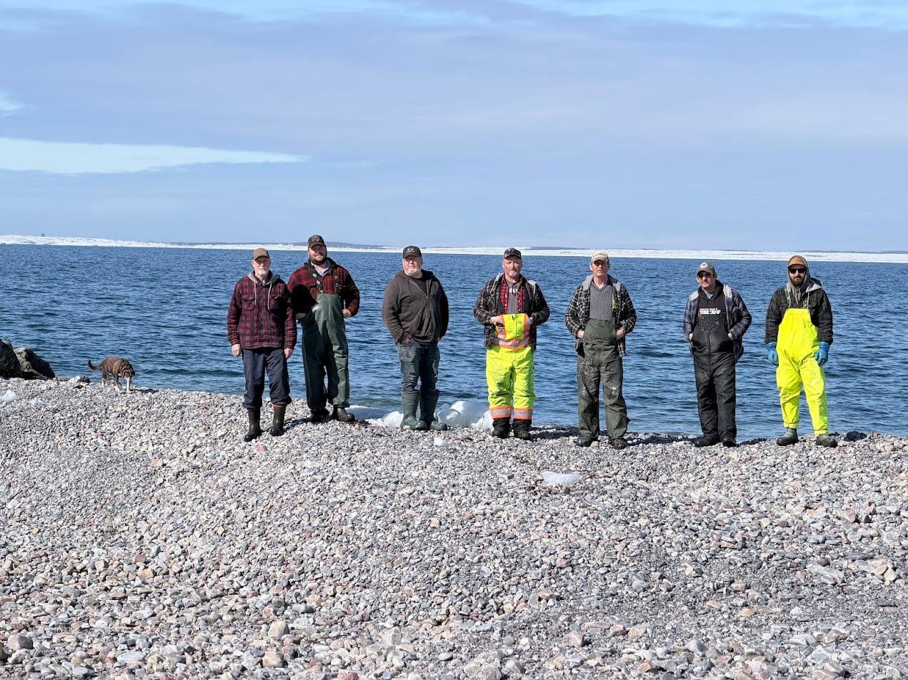 A group of men standing on a pile of rock in the ocean.