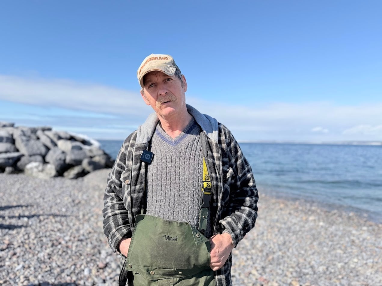 A man wearing a hat and overalls stands on a beach.