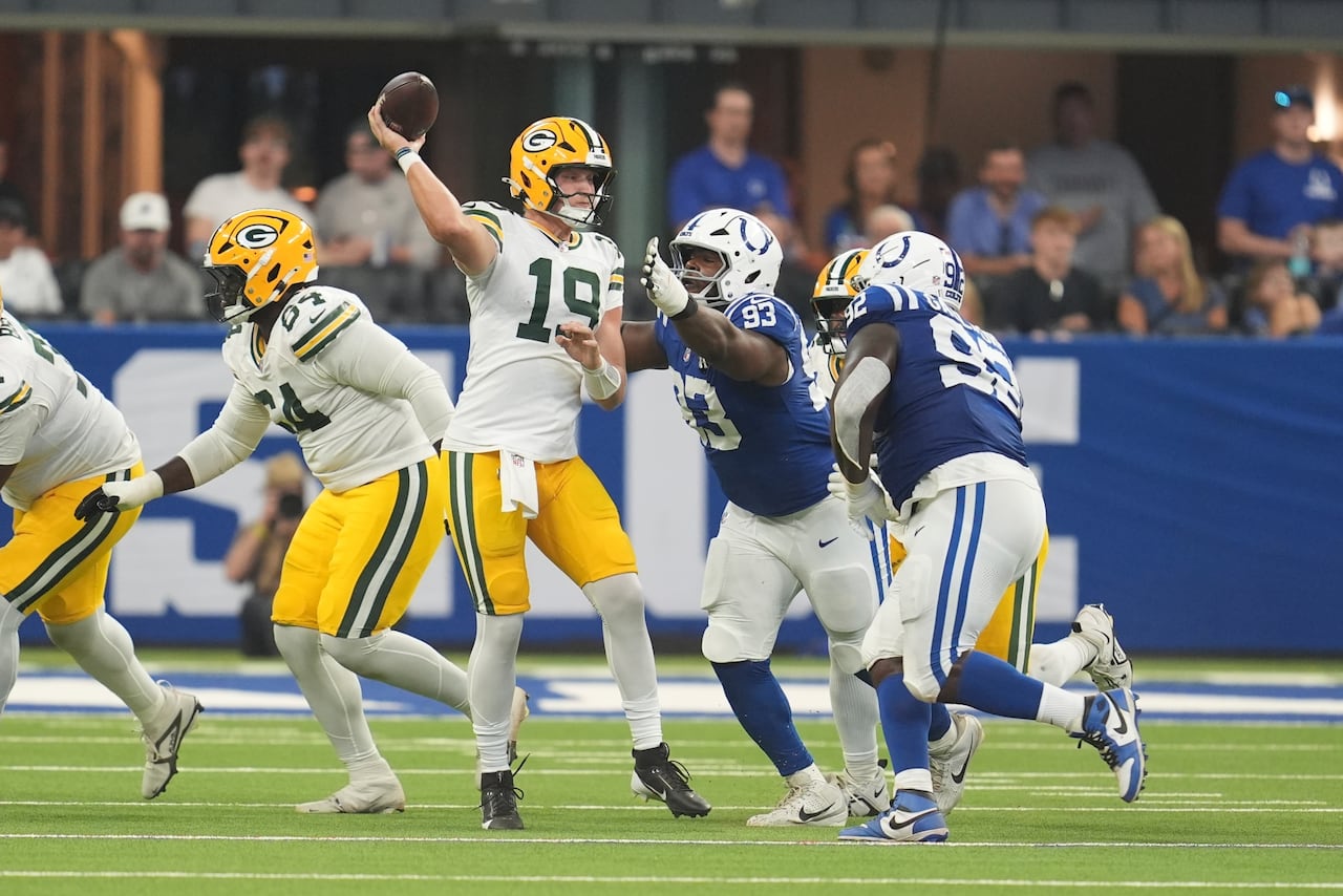 A quarterback throws the ball while being rushed by two opposing players.