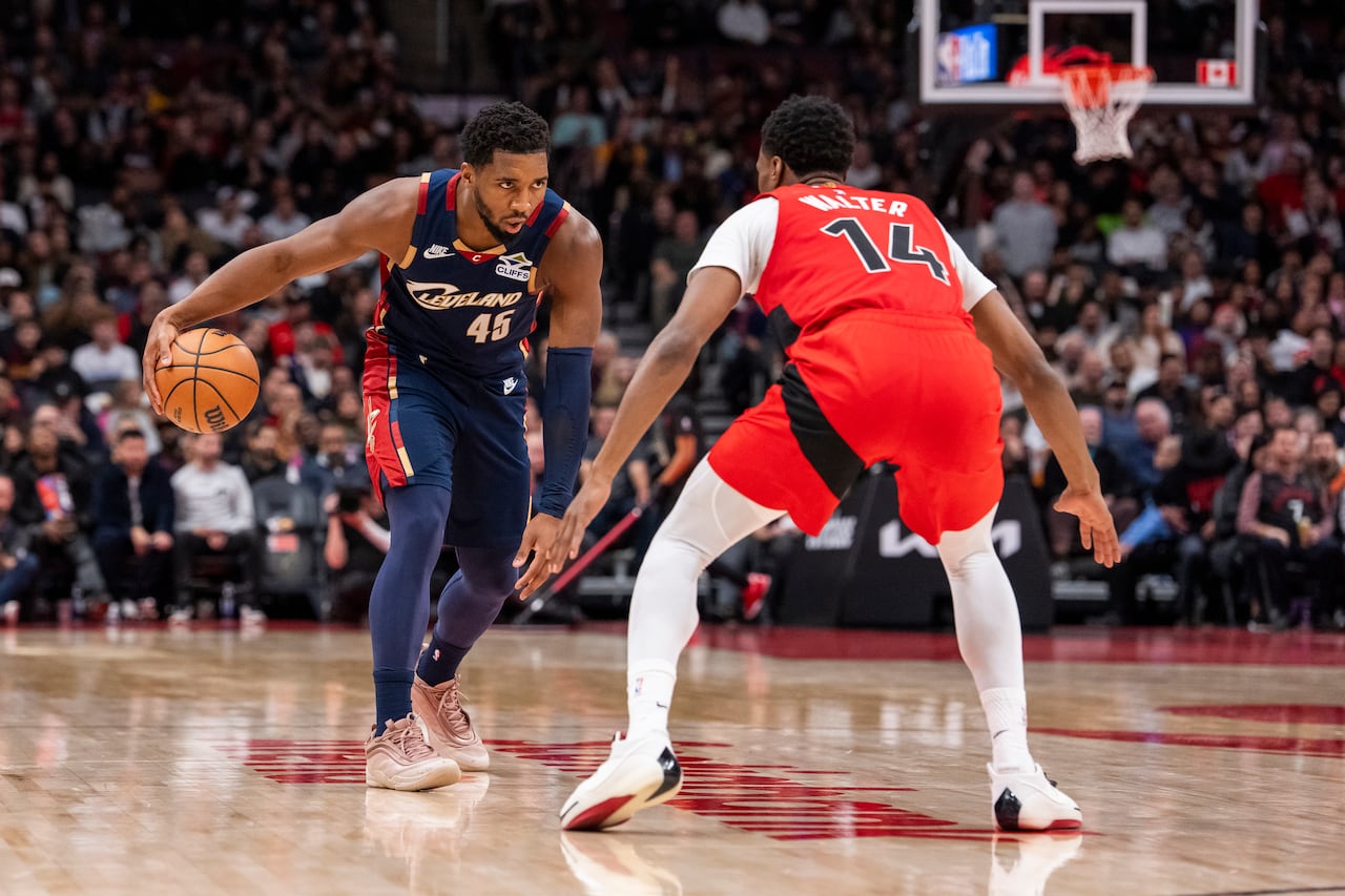 Donovan Mitchell of the Cleveland Cavaliers dribbles a basketball while being guarded by Ja'Kobe Walter of the Toronto Raptors