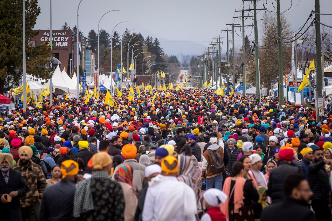 Thousands of people are pictured marching down a wide street, waving yellow flags. There are white tents on the side. 