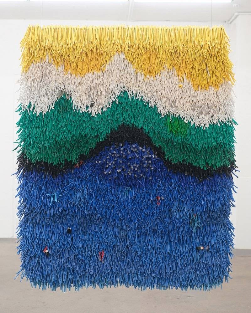 Hanging artwork of fringe in bands of blue, green, yellow and white.