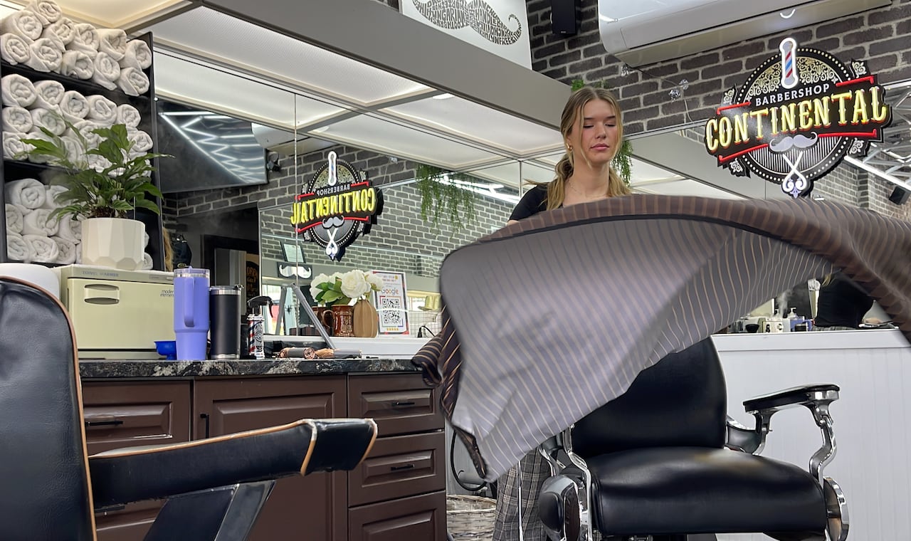 A woman shakes out a bib in a barber shop.