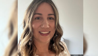Kaitlyn Soron wears a lacy blouse with her hair loosely curled around her face. She smiles at the camera