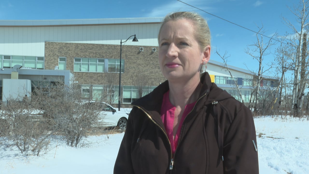 A woman looks off camera on a sunny day, with a snow-covered street in the background.