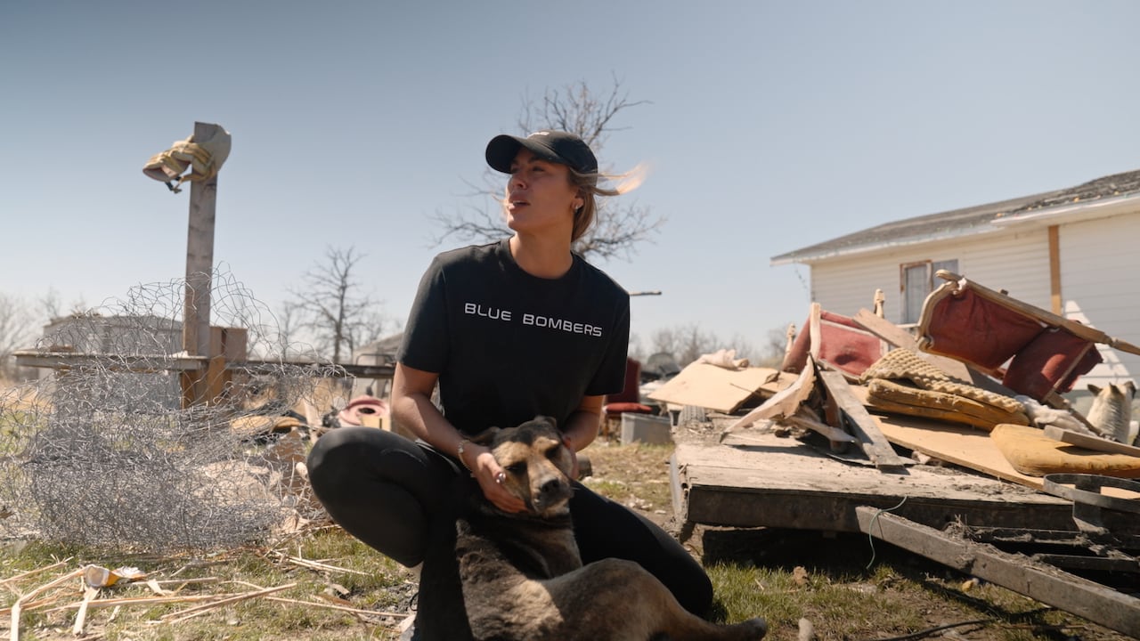 A woman comforts a dog in front of a damaged home.