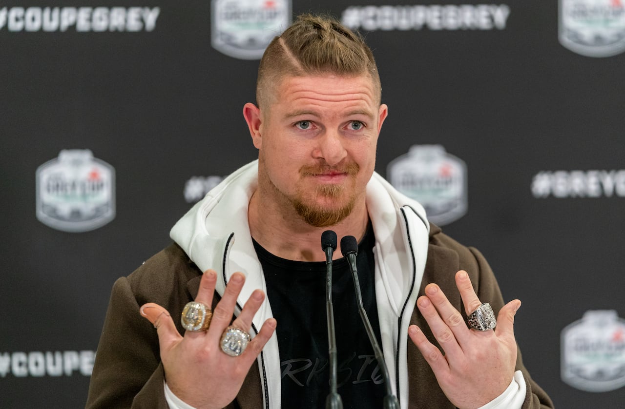 A football player in street clothes holds up his hands to show championship rings on his fingers.