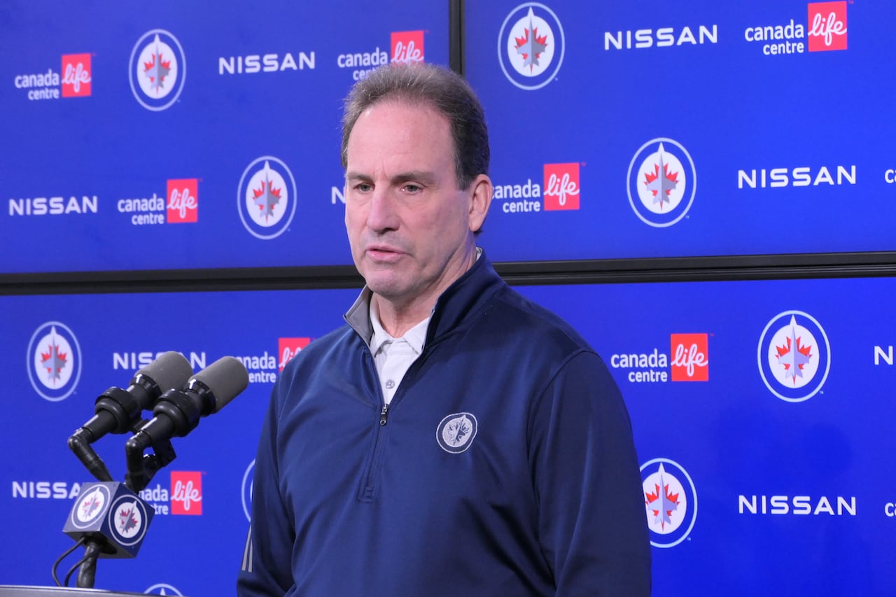 A man speaks at a podium with a blue Winnipeg background behind him.