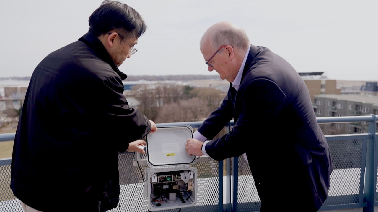 Cheol-Heon Jeong and Greg Evans hold a square pollution monitoring instrument attaching it to the roof of a building in the Bathurst Quay community.