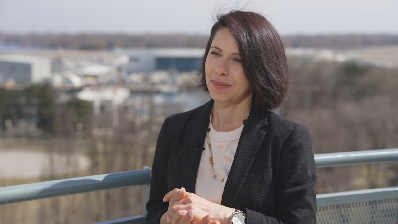Marianne Hatzopoulou stands holding her hands wearing a black blazer and necklace.
