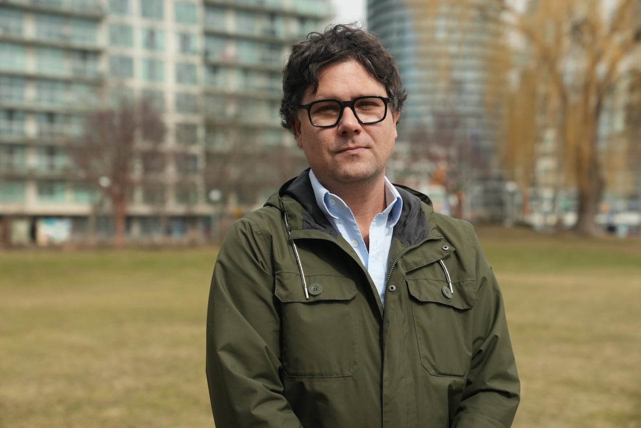 Scott Weichenthal wears a green rain coat and stands in park in Bathurst Quay