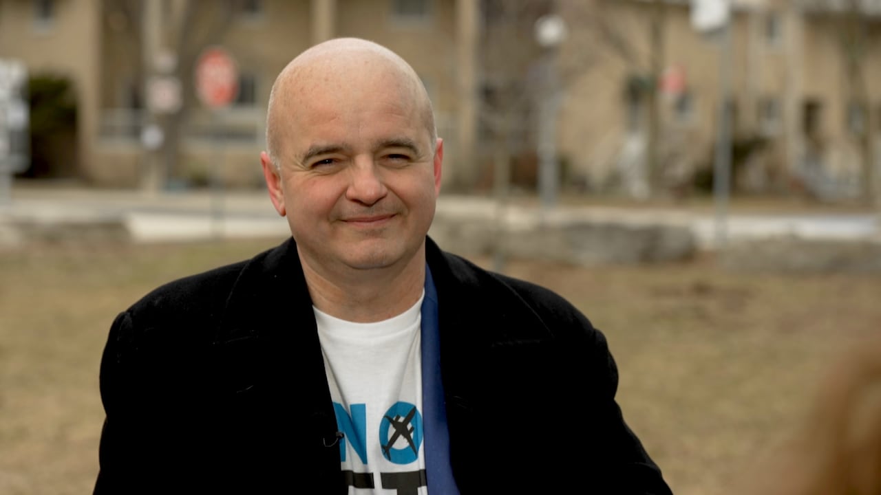 Norm Di Pasquale sits at a bench in the Bathurst Quay neighbourhood wearing a NoJetsTO t-shirt and black blazer.