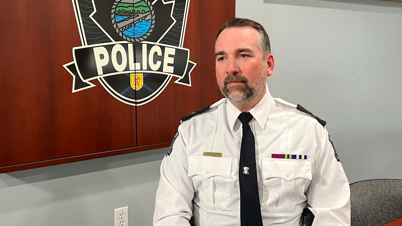 A white man with brown hair and a short brown beard in a white collared police uniform and tie.