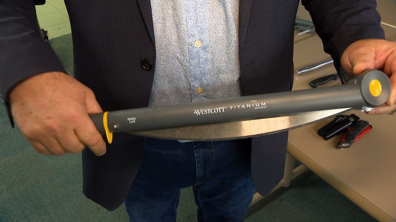 A man holds what was once the arm of a paper cutter, but has since been converted into a weapon.