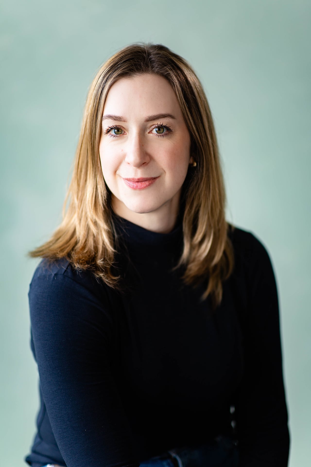 A woman with shoulder length blond hair is wearing a navy blue sweater and looking directly at the camera.
