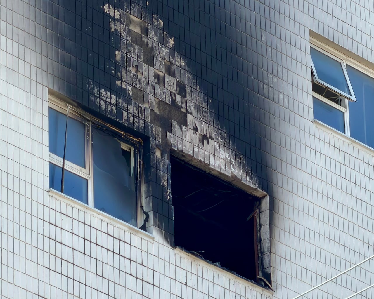 A closeup shows black smoke marks on the side of a white building around an open window.