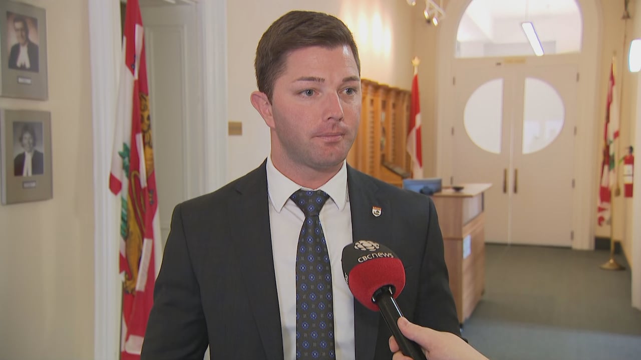 A man in a dark suit and white shirt taking questions from a reporter.