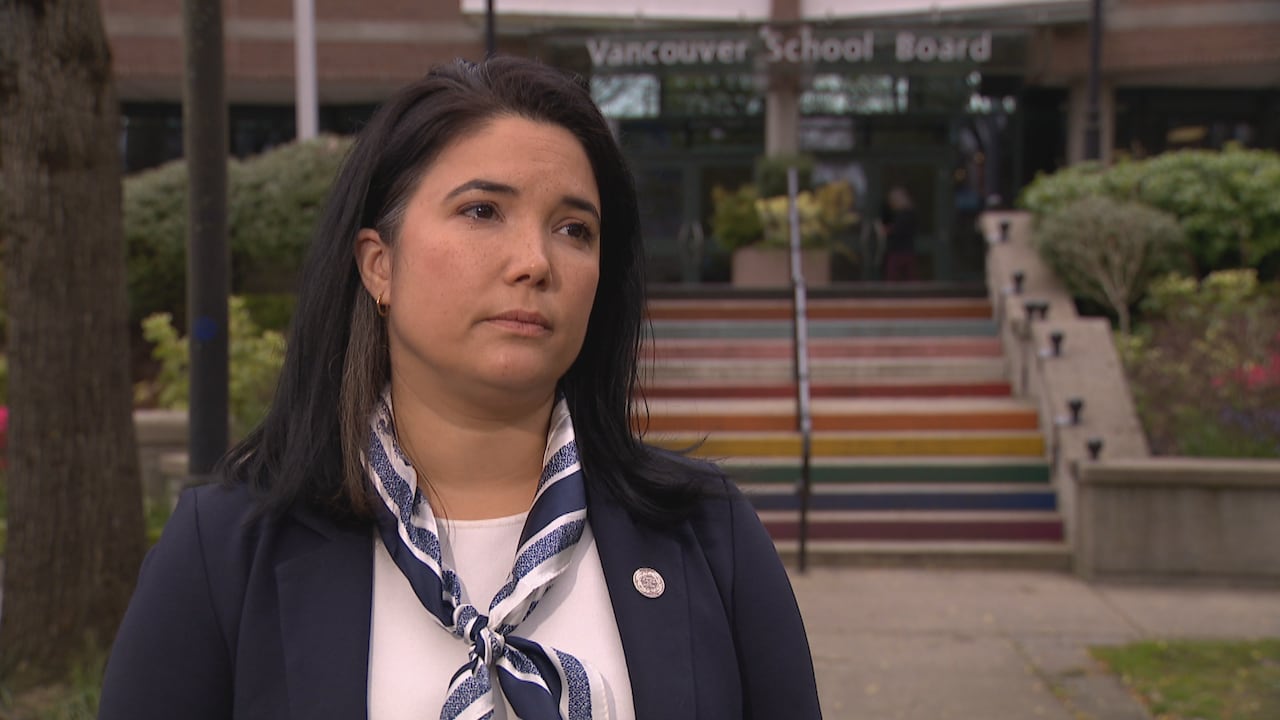 A woman wearing a blazer and neck scarf is seen in front of rainbow-patterned steps.
