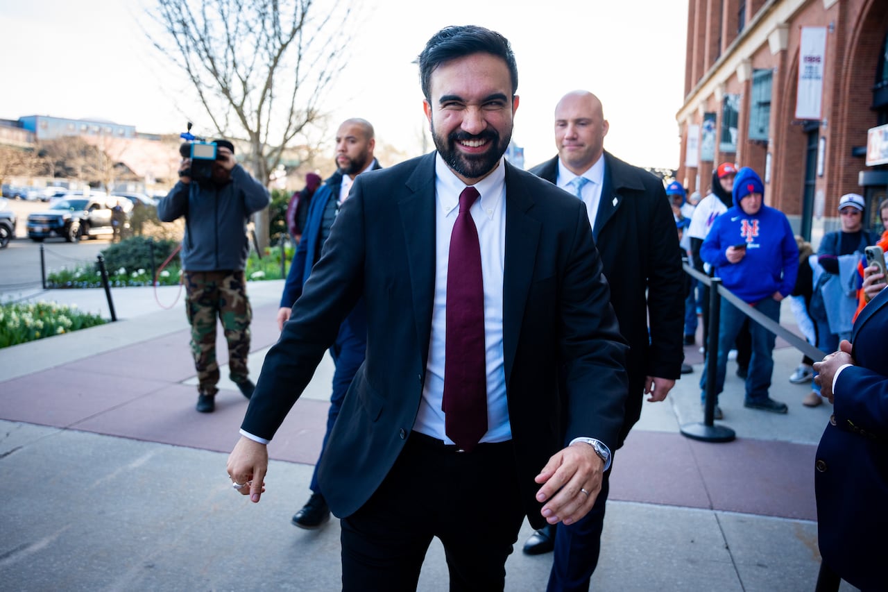 A man in a suit walks down a sidewalk while being followed by several other people.