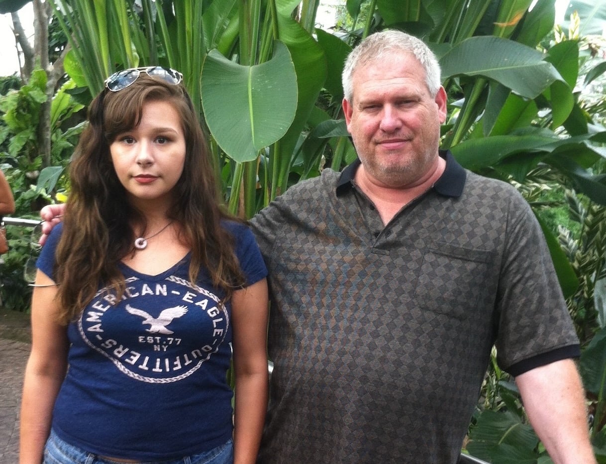 A man and a young woman stand among tropical trees.