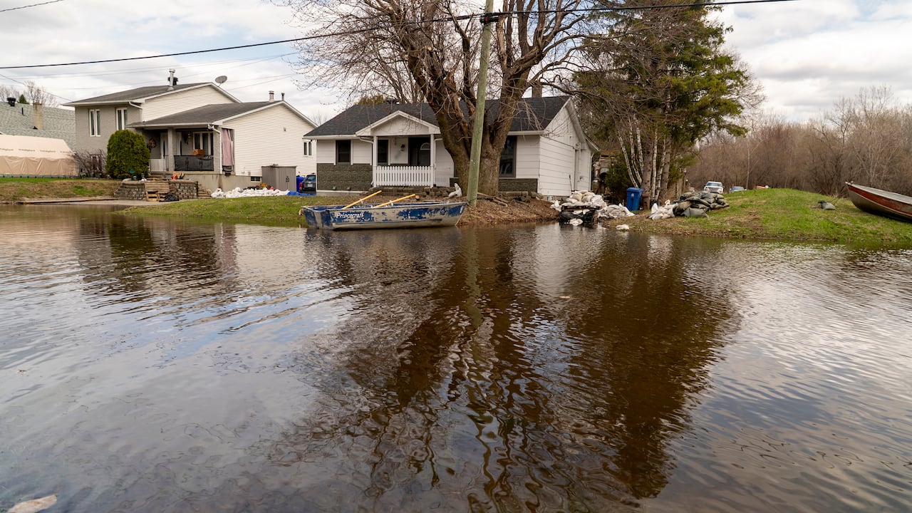 Photo of water submerging a street and a rowing-boat docking on the front yard of a houses