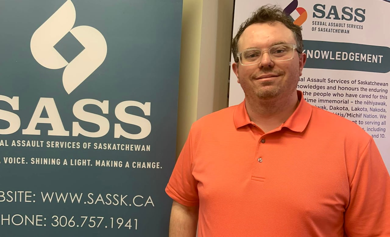 A man in a salmon shirt stands next to a sign.
