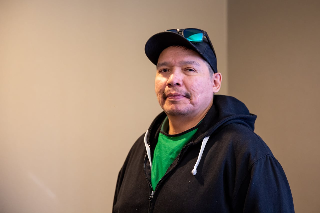 A person wearing a hoodie and a ballcap is seen standing in a hallway.